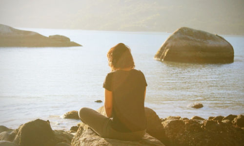 woman pensive sitting on a rock looking at the ocean