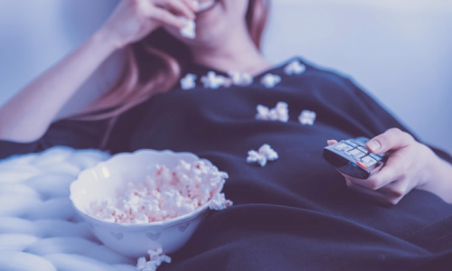 woman eating popcorn with remote in hand