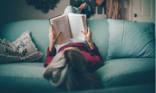 woman lying in sofa reading a book