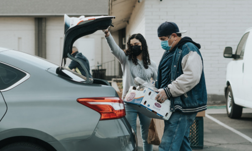 a male helping a woman to put a box in the trunk of her car