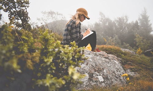 woman sitting on a rock in nature writing in a journal