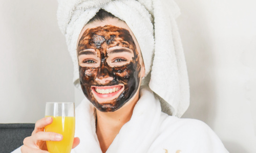 woman at the spa treating herself wearing charcoal mask and robe