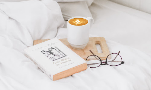coffee, book and prescription glasses on bed
