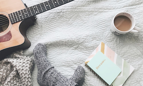 woman sitting on blanket with guitar, journal and coffee