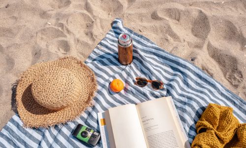 straw hat book cold drink sunglasses laid out on a towel on the beach