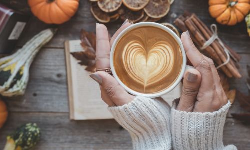 woman drinking hot chocolate surrounded by cinnamon & pumpkin