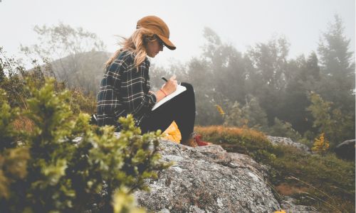 woman sitting outdoors writing in journal