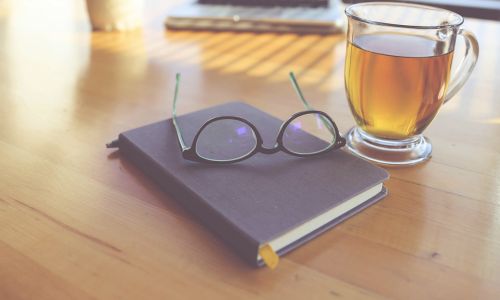 journal, glasses and a cup of tea on a table