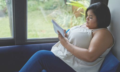 woman sitting by window writing in journal